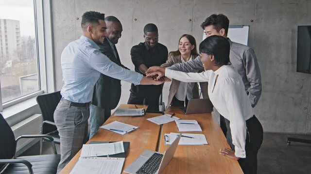Multi-ethnic businesspeople business team group of co-workers colleagues putting their hands on top of each other making teamwork gesture showing unity partnership applaud clapping standing in office 