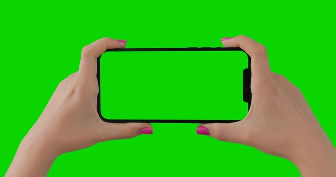 Close up of woman hands with pink manicure holding horizontal smartphone with green screen. Isolated chroma key mobile Apple iPhone 12 Pro Max perfect for product placement.
