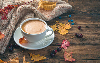 Autumn morning, a cup of coffee, foliage and a sweater on a wooden background. Side view, space for copying. Tinted image.