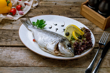 Steamed dorado on plate with lemon on old wooden table