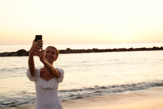 Happy beautiful woman taking selfie with mobilephone on the beach during sunset time.