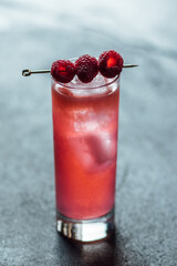 raspberry cocktail in tall Collins glass with ice and raspberries on cocktail pick