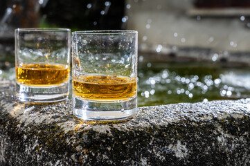Glasses of strong scotch single malt whisky served on old stone reservoir for water from mountain spring