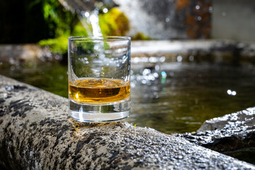 Glass of strong scotch single malt whisky served on old stone reservoir for water from mountain spring