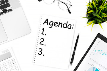 Text AGENDA on notebook. Laptop, calculator, clipboard for chart, glasses, pen and plant. Flat lay, Business concept.