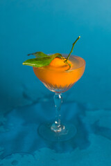 mandarin tangerine dropping into cocktail drink glass splash wet accident blue background