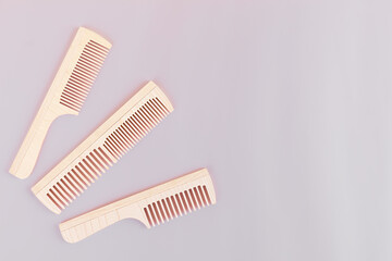 Three natural wood combs on a lilac background with copy space, top view. Eco-friendly accessories for combing hair.