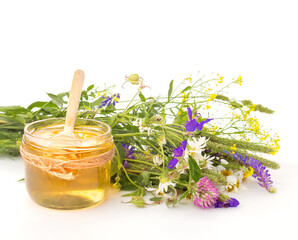 Flower honey. Glass jar of honey with wooden honey dipper, a bouquet of  wildflowers against white background isolated, close-up, front view.