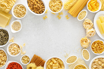 Fototapeta na wymiar Pasta. Various kinds of uncooked pasta and noodles over stone background, top view with copy space for text. Italian food culinary concept. Collection of different raw pasta on cooking table