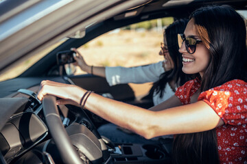 Pretty young women taking a photo while driving a car on road trip on beautiful summer day.