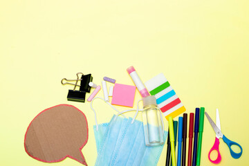 Back to school, school supplies and chat cardboard bubble with medical mask and gel on a yellow background. Protection of schoolchildren and students from the virus