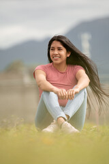 smiling hispanic girl sitting in a green area, concept of freedom