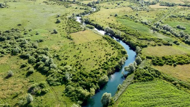 Aerial drone view of river flowing in nature. Beautiful river, field and trees in summer. Klokot river, Bosnia and Herzegovina.
