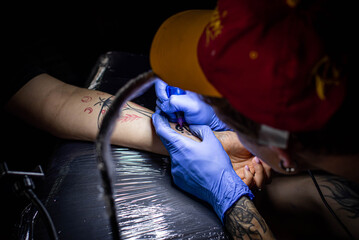 cropped shot of tattooing process on hand in salon. A professional tattoo artist introduces ink into the skin using a needle from a tattoo machine.Professional tattooist working in studio.