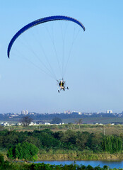 pilot flying motorized paraglider over lake in city park