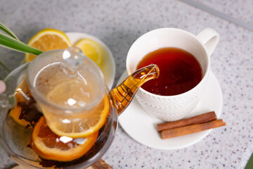 A hot tea drink with lemon and orange, a teapot and a white cup, served with delicious lemon and cinnamon. Fragrant and warming tea. Step 3