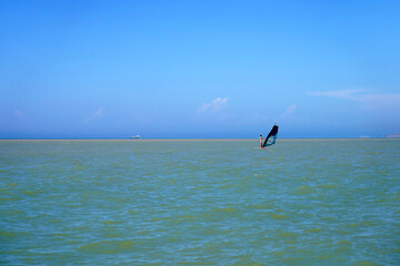 A lonely man on a wind surf trying to catch the wind with a sail, a windsurfer against the...