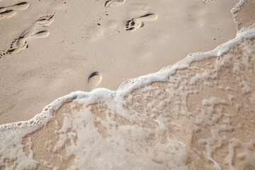 Footprints of bare feet are over a wet sand on the beach