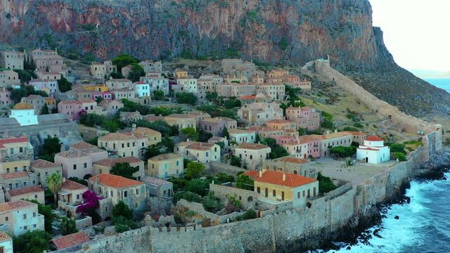 Aerial of the small ancient village Monemvasia in Greece. The village is settled on a hillside, facing the ocean. The drone pans over the village and then fly backwards. It is a beautiful sunny summer