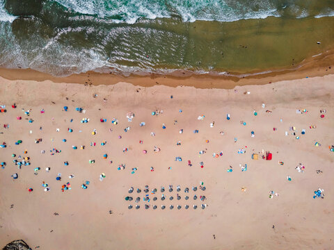 Aerial view of Praia de Odeceixe with people on the beach in summertime with Atlantic Ocean rough sea in background, Odeceixe, Faro, Portugal.