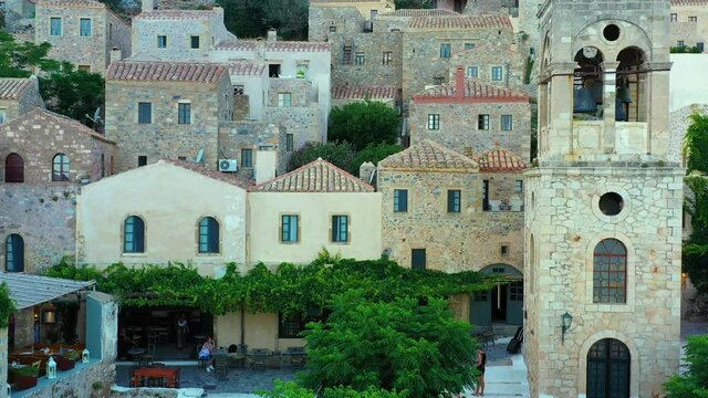 Aerial of the small ancient village Monemvasia in Greece. The village is settled on a hillside, facing the ocean. The drone fly rises up over the village, from a start position on a small town square.