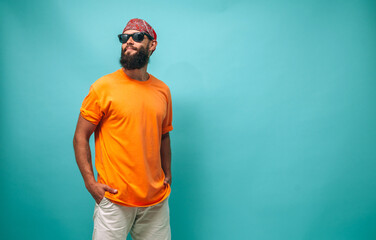Portrait of a young bearded hipster guy wearing red bandana and orange blank t-shirt stands against...