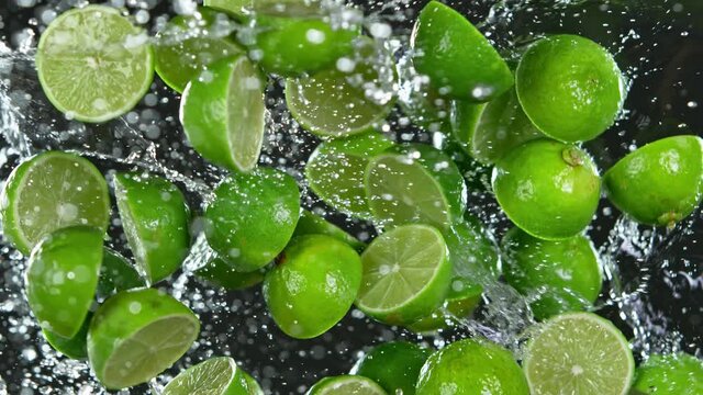 Super Slow Motion Shot of Flying Fresh Limes and Water Side Splash Isolated on Black at 1000 fps.