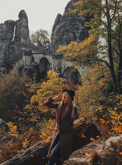 Girl in a hat on the background of the bastei bridge in saxon switzerland autumn, yellow leaves