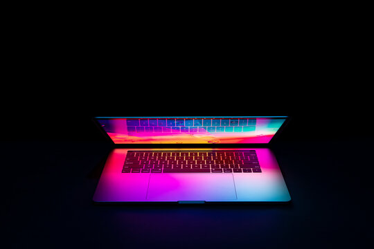 Isolated high tech open laptop with abstract vibrant color screen on a dark background.
