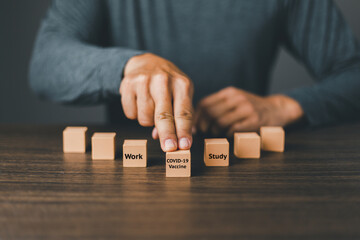 Hand of a man choose Wooden cube block with word covid-19 vaccine first before work and study. Process for the healthy concept.