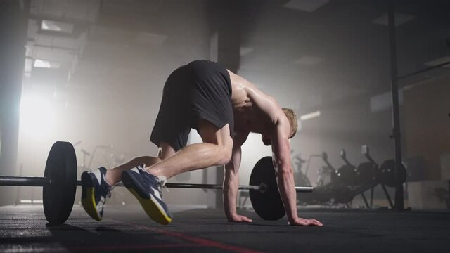 Fitness man doing burpee workout at gym. Medium shot of young man doing push ups and jump exercise in slow motion. Sport concept