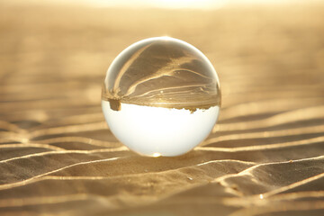 Fototapeta na wymiar Clear crystal ball are sphere reveals seascape view with spherical placed on the sand beach during sunset.