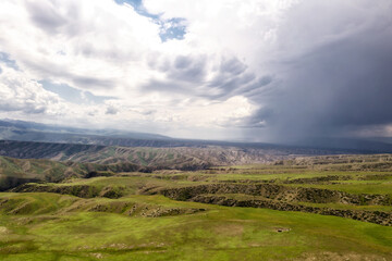 Mountain peaks and grassland are under white clouds.