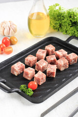 Raw Saikoro Wagyu Cubes Beef Steak on Steak Plate with Lettuce at Background, Above White Table with other Spice at Background