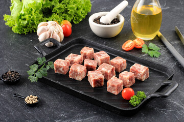 Raw Frozen Saikoro Wagyu Cubes or Dice Beef Steak on Black Steak Plate with Spice and Vegetable
