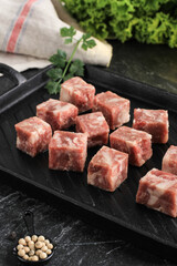 Raw Frozen Saikoro Wagyu Cubes or Dice Beef Steak on Black Steak Plate with Spice and Vegetable