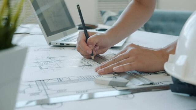 Close-up of female hands drawing on blueprint while architect is working at home using laptop. Contemporary activities and professions concept.