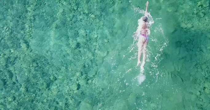 Swim training concept: Drone air view of a person swimming in crystal clear waters.  Professional aquatic training for Olympics. Sport exercise and strength building on sea background with copy space