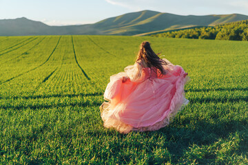 Girl in pink dress walking through green fields at sunset