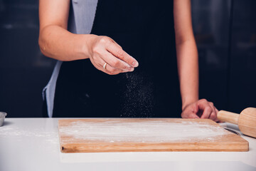 Hands of baker woman female making sprinkling flour dough on table
