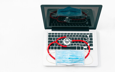 Top view of a laptop with a stethoscope and a surgical mask over its keyboard