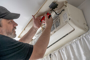 Professional air conditioning technician cutting the internal control cables of an internal unit of a split air unit to replace it with a new one.