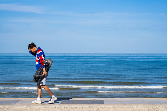 Man teennager wearing sportwear and shoes playing,walking and holding surf skate on the road oudoor in the morning. Relax and enjoy extreme surfskate on summer holiday at the beach.
