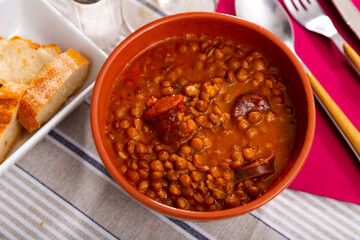 Stewed lentils with chorizo and vegetables with thick tomato sauce served in earthenware bowl. Typical Spanish cuisine