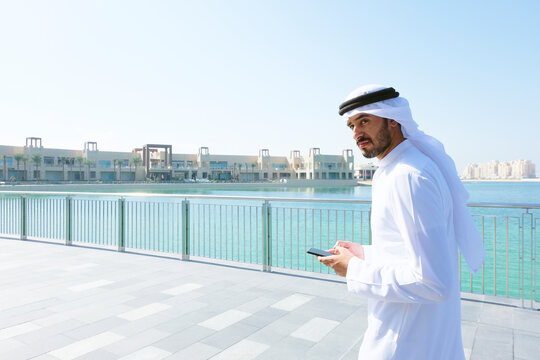Arabic man using mobile smart phone. Emirati on Kandura holding a device while checking online websites, eCommerce or blogs