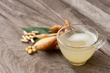 Glass cup of finger root hrbal tea and finger root (Chinese Ginger, Galingale, Kaempfer, Boesenbergia rotunda, Krachai) with green leaf isolated on wooden table background.