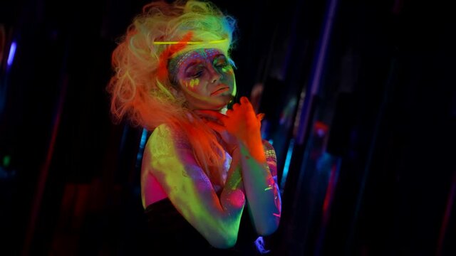 fluorescent cosmetic is glowing in darkness, model with bright paints on skin and hair