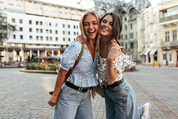 Young female friends in stylish jeans and floral trendy blouses hug, smile and pose in great mood...
