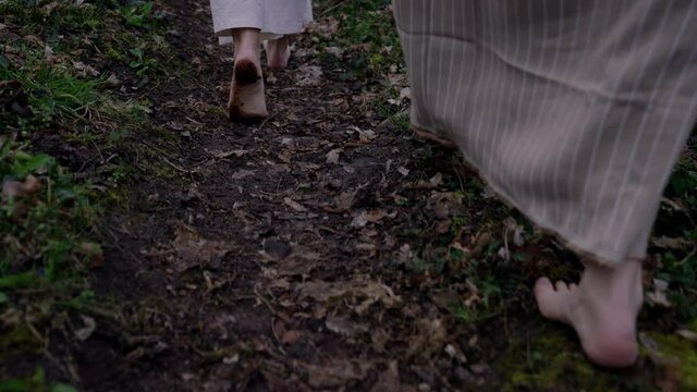 barefooted women walking on a path early in the morning with white robes and jars in their hands.