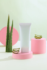 Green Background with natural cosmetics of aloe vera, fresh leaves of aloe on bright green and podium geometrical pink. Blank white cosmetic skincare makeup containers